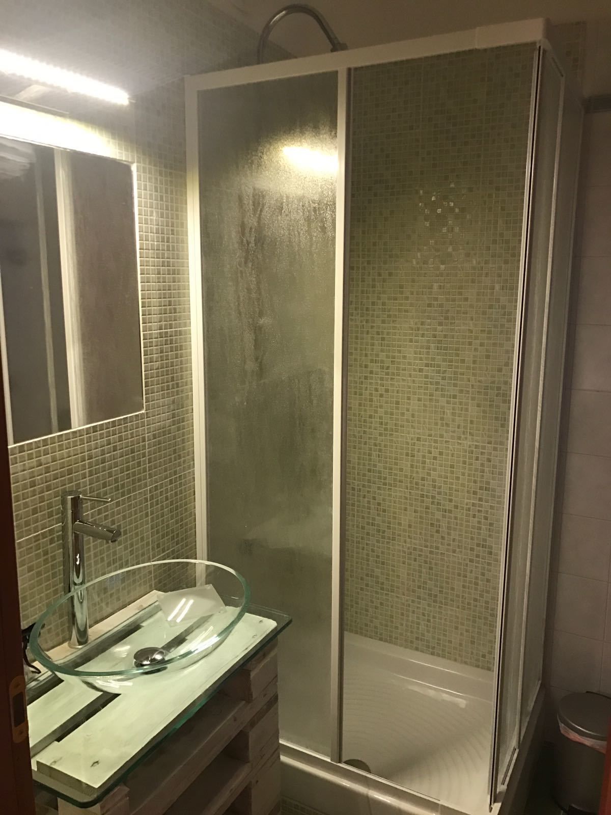 Une salle de bain moderne avec un lavabo en verre, un espace douche et un mur recouvert de carreaux.