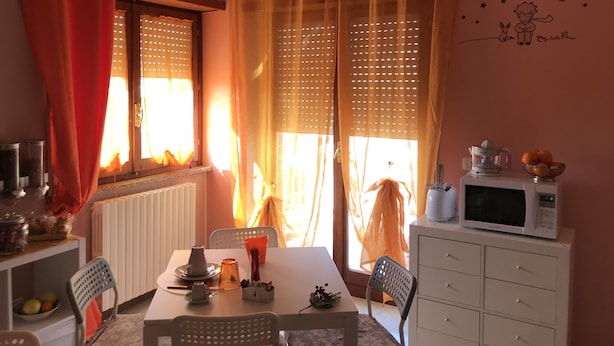 Un comedor con una mesa, sillas, microondas y ventana con cortinas.
