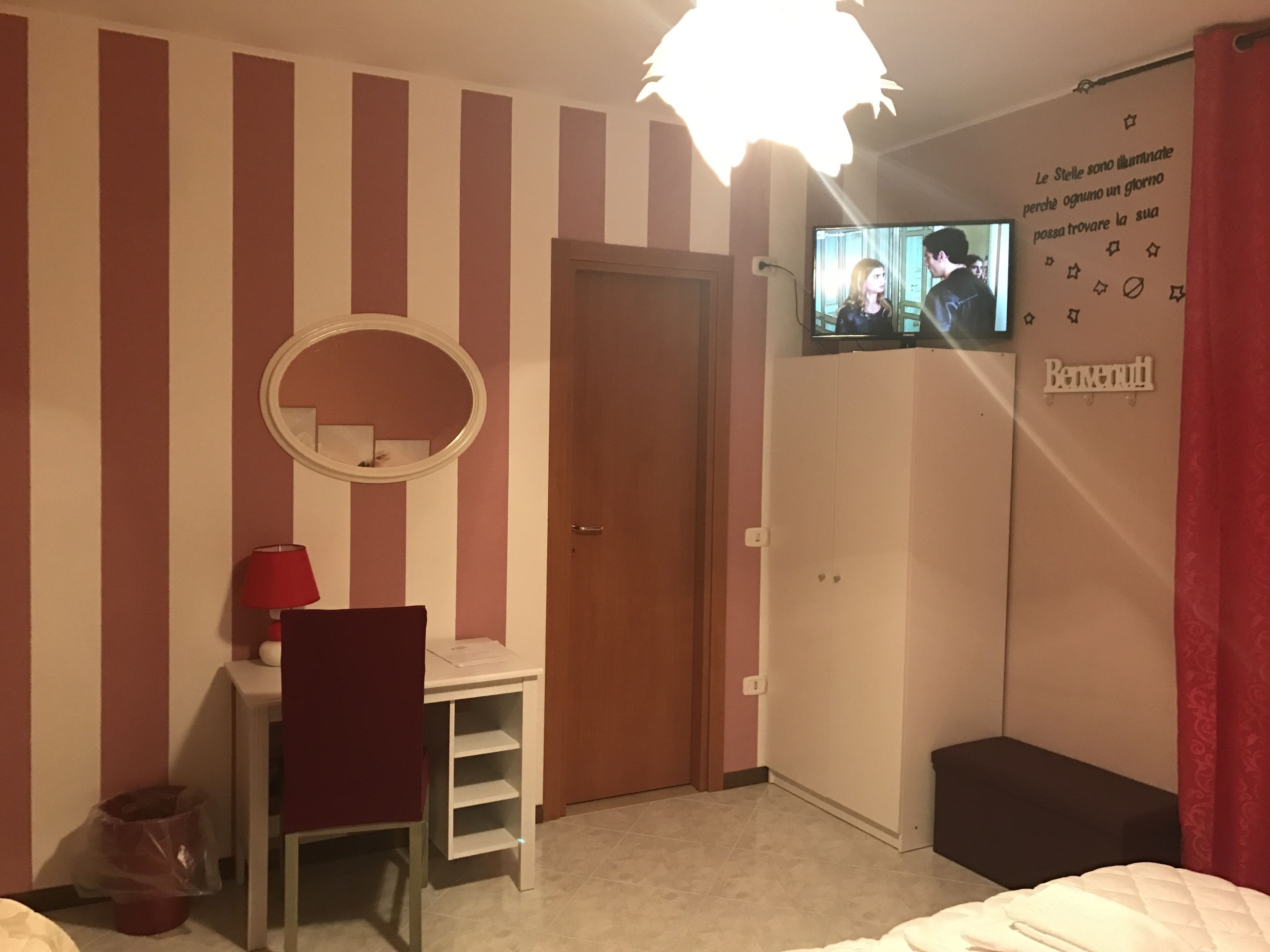 Ett sovrum med randiga väggar, ett skrivbord med en stol, en säng, en tv som är monterad på väggen och en spegel.