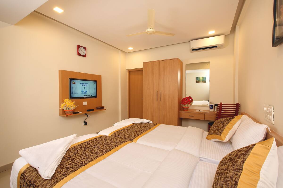 A hotel room with two beds, a TV, a wardrobe, and a mirror.
