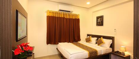 A hotel room with a bed, a desk, a chair, a plant, and a ceiling fan.