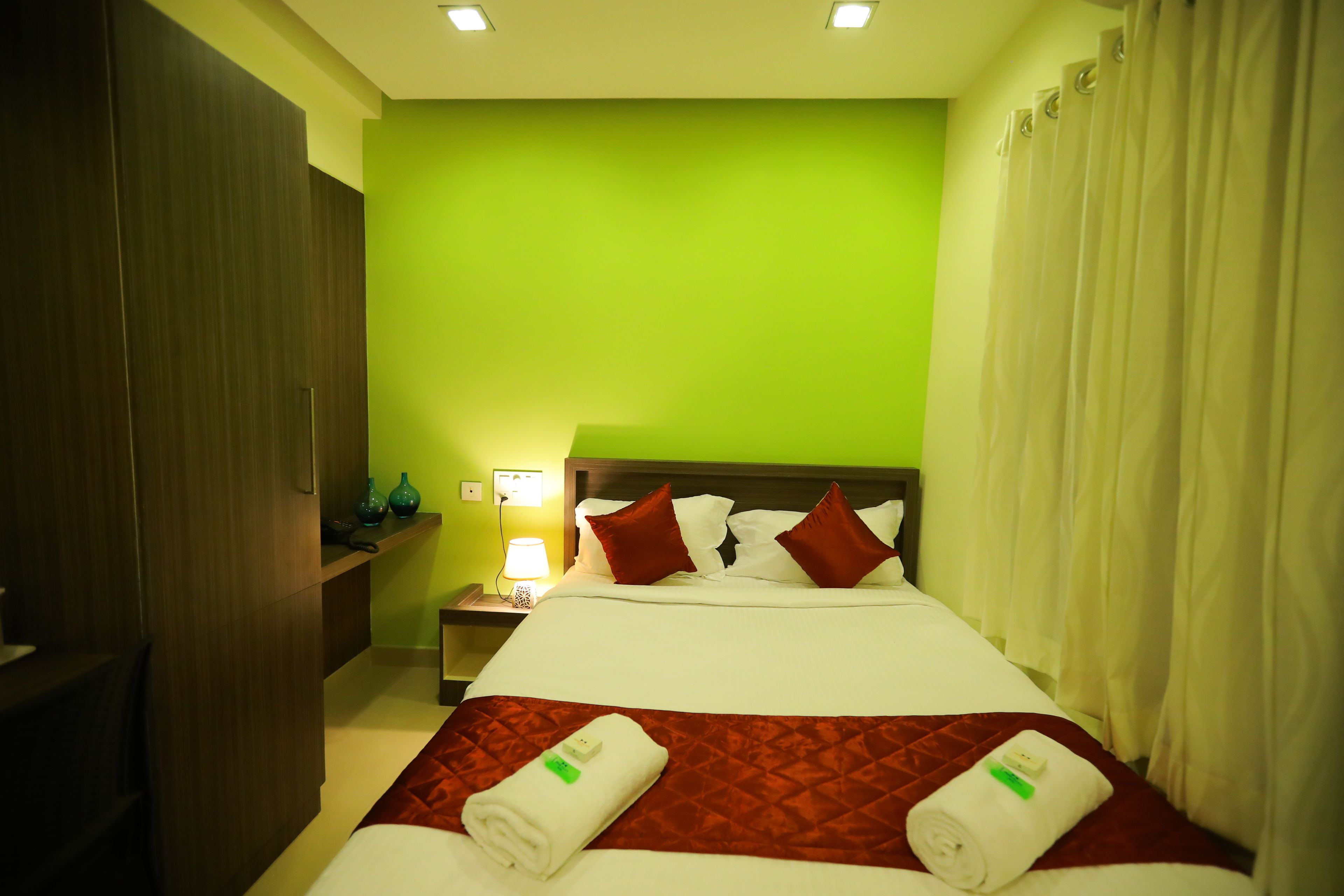 Une chambre d’hôtel avec un lit, une table de chevet, une lampe et un mur vert.