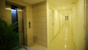 Um corredor moderno com piso brilhante, elevador embutido na parede e uma porta no final.