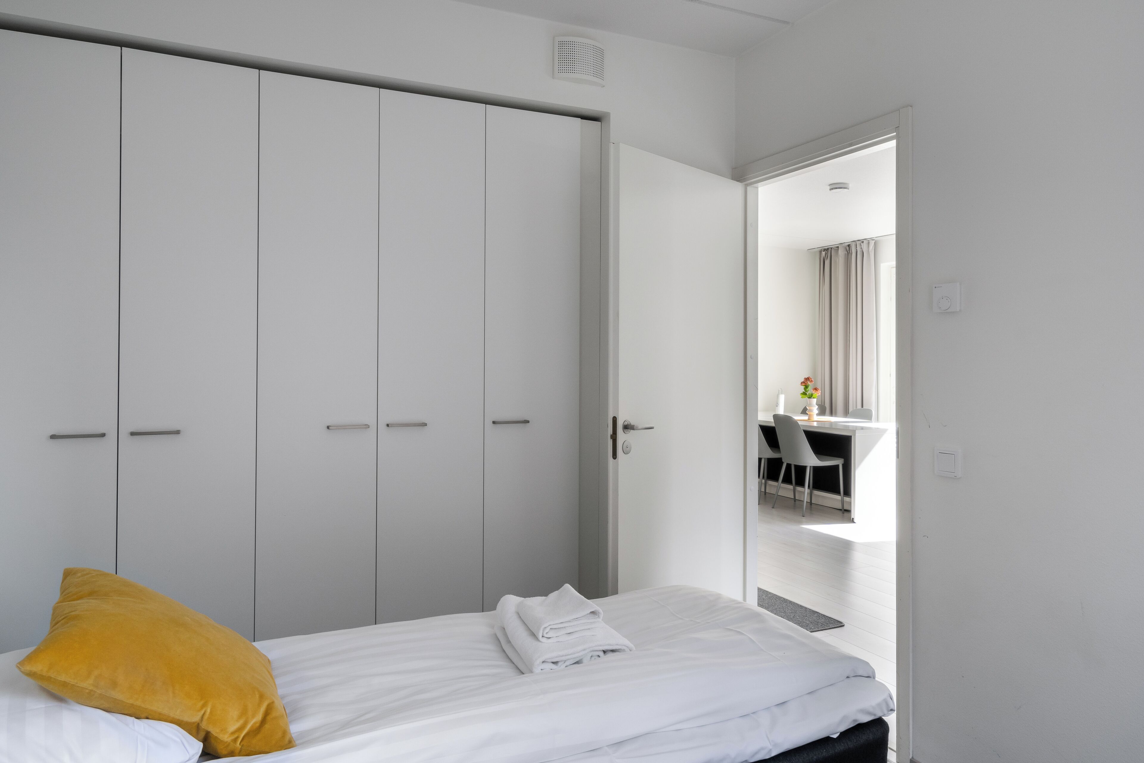 A bedroom with a bed, a yellow pillow, a wardrobe, and a desk with a chair.