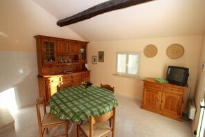 Une cuisine avec une table à manger, des placards en bois, un téléviseur et une fenêtre.
