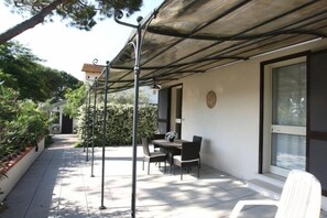 An outdoor patio with a table and chairs, a covered area, and a white chair. - Agriturismo Peretti (Orbetello)