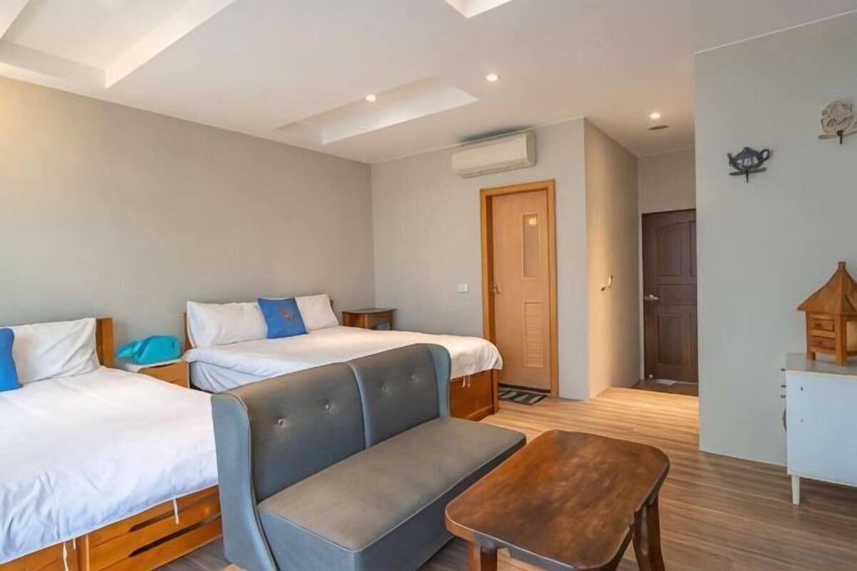 Ein Zimmer mit zwei Betten, einer Bank, einem Holztisch und einer Tür zu einem anderen Raum.