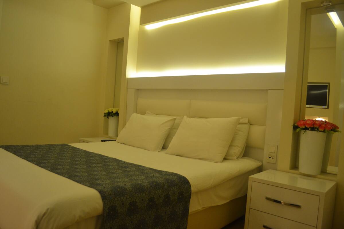 A hotel room with a large bed, a bedside table with a lamp, and a mirror.