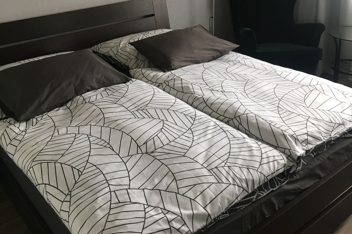 Una cama bien hecha con ropa de cama estampada, un cabecero moderno y un cuadro geométrico y colorido en la pared.
