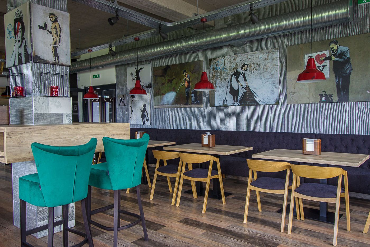 Een restaurantinterieur met turquoise stoelen, houten tafels en rode hanglampen.