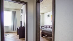 A hotel room with a wooden floor, a bed with a patterned bedspread, a television on a stand, and a window with curtains. - Hotel & Bistro 63 (Poprad)