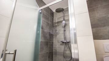 A shower with a handheld showerhead and a wall-mounted faucet, a glass shower door, and a tiled wall with a mix of light and dark tiles.