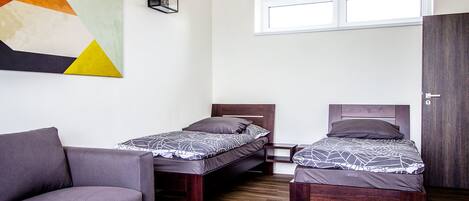 Habitación compacta con dos camas individuales, un sofá, una mesita y una obra de arte geométrica en la pared.