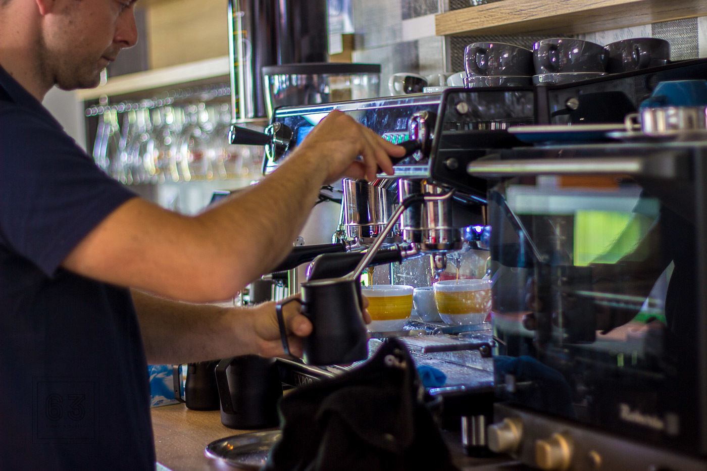 Una persona usando una máquina de café, con varias tazas y una espumadera de leche a la vista.