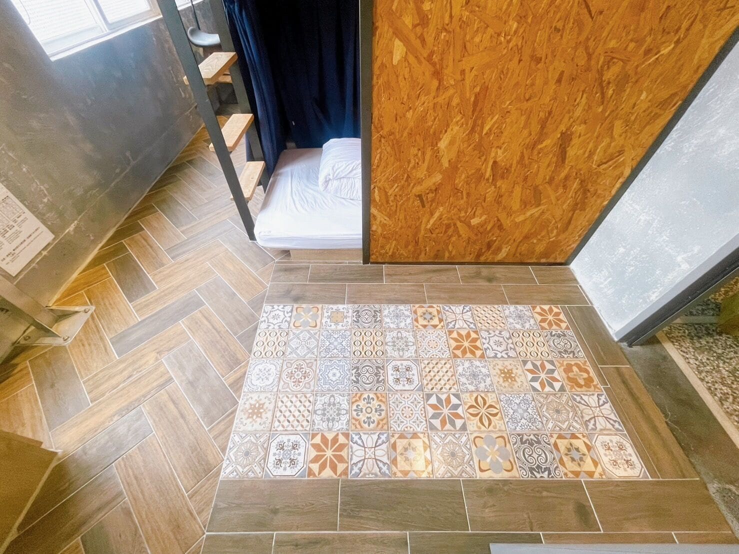 A room with a herringbone patterned floor, a bed with white bedding, and a wooden partition.
