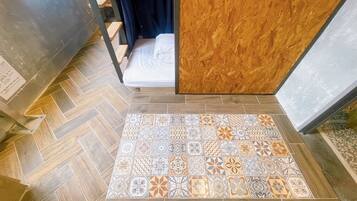 A room with a herringbone patterned floor, a bed with white bedding, and a wooden partition.