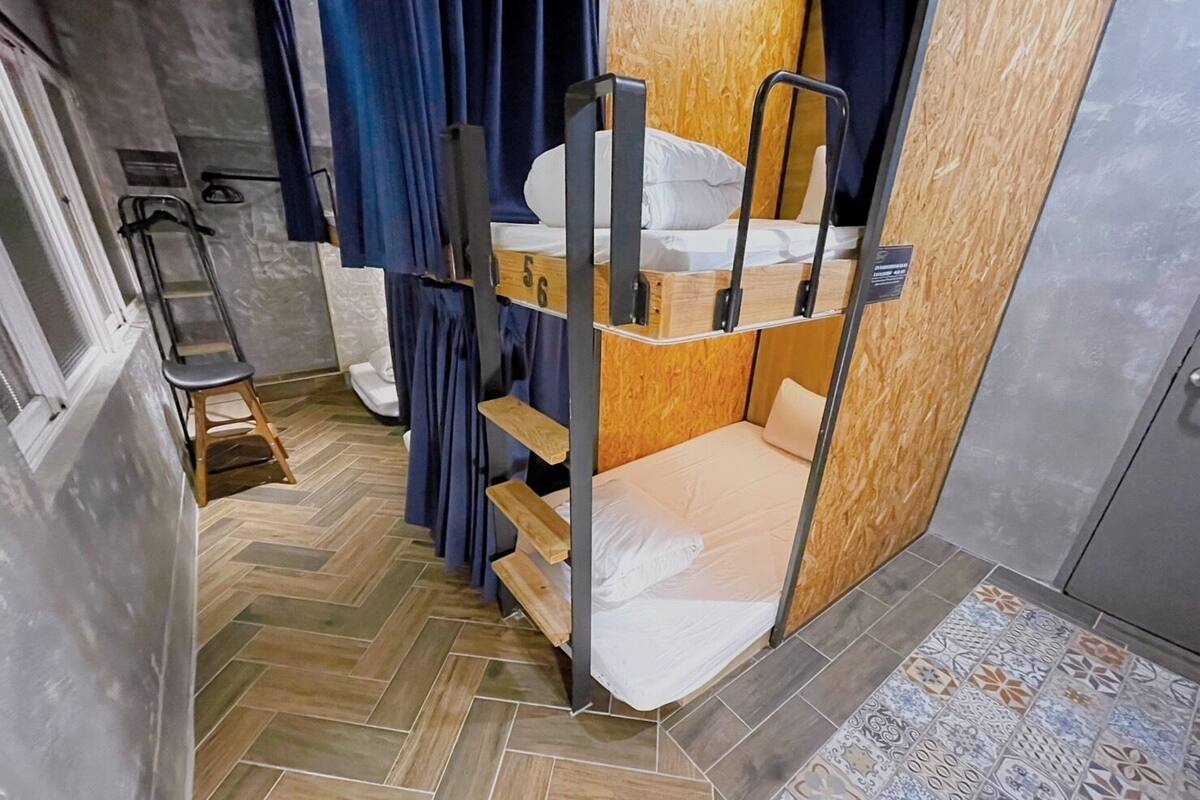 A bunk bed room with a herringbone floor pattern, a wooden door, and a small stool.