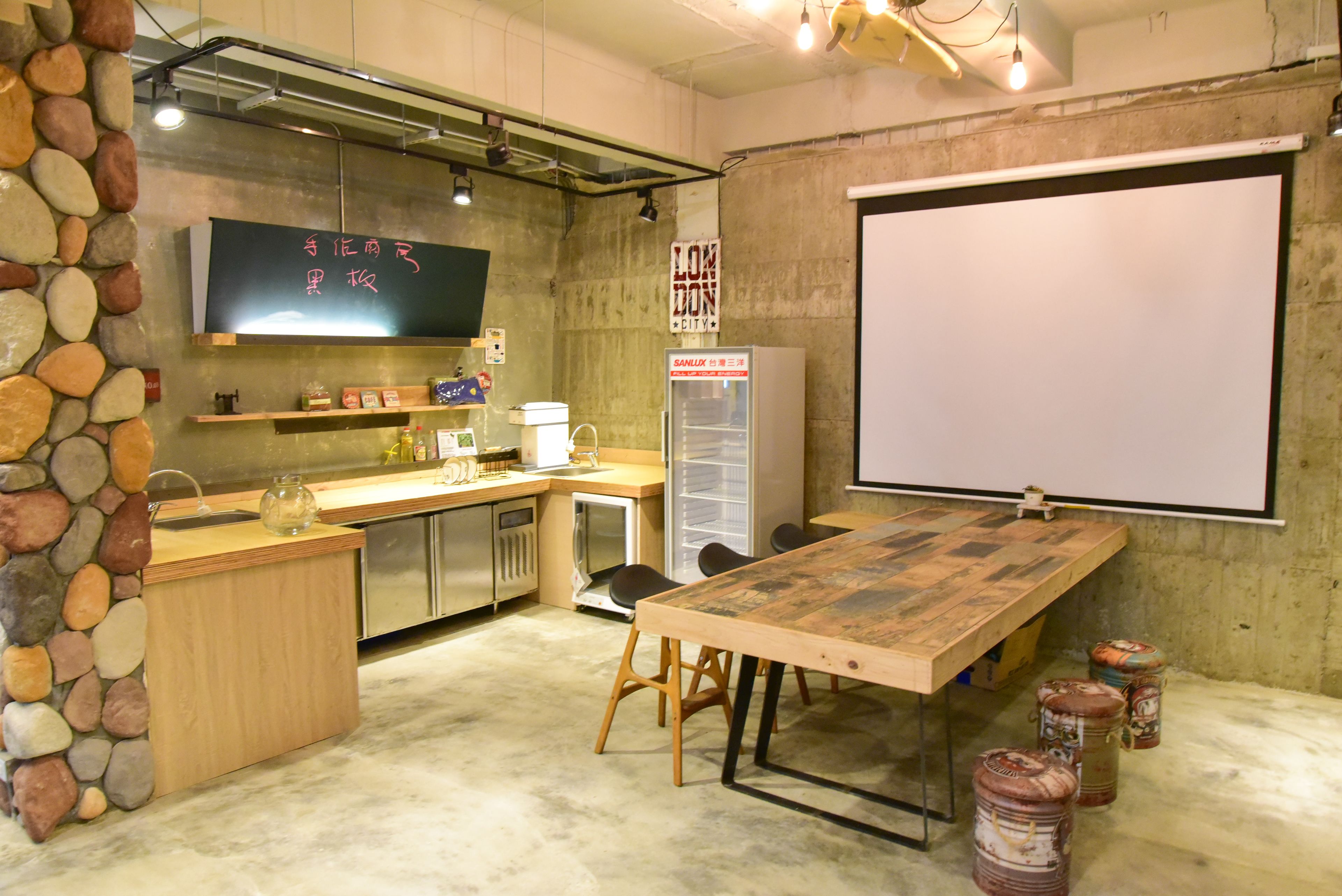 Una cocina con una mesa de madera, taburetes, una pizarra y un refrigerador.