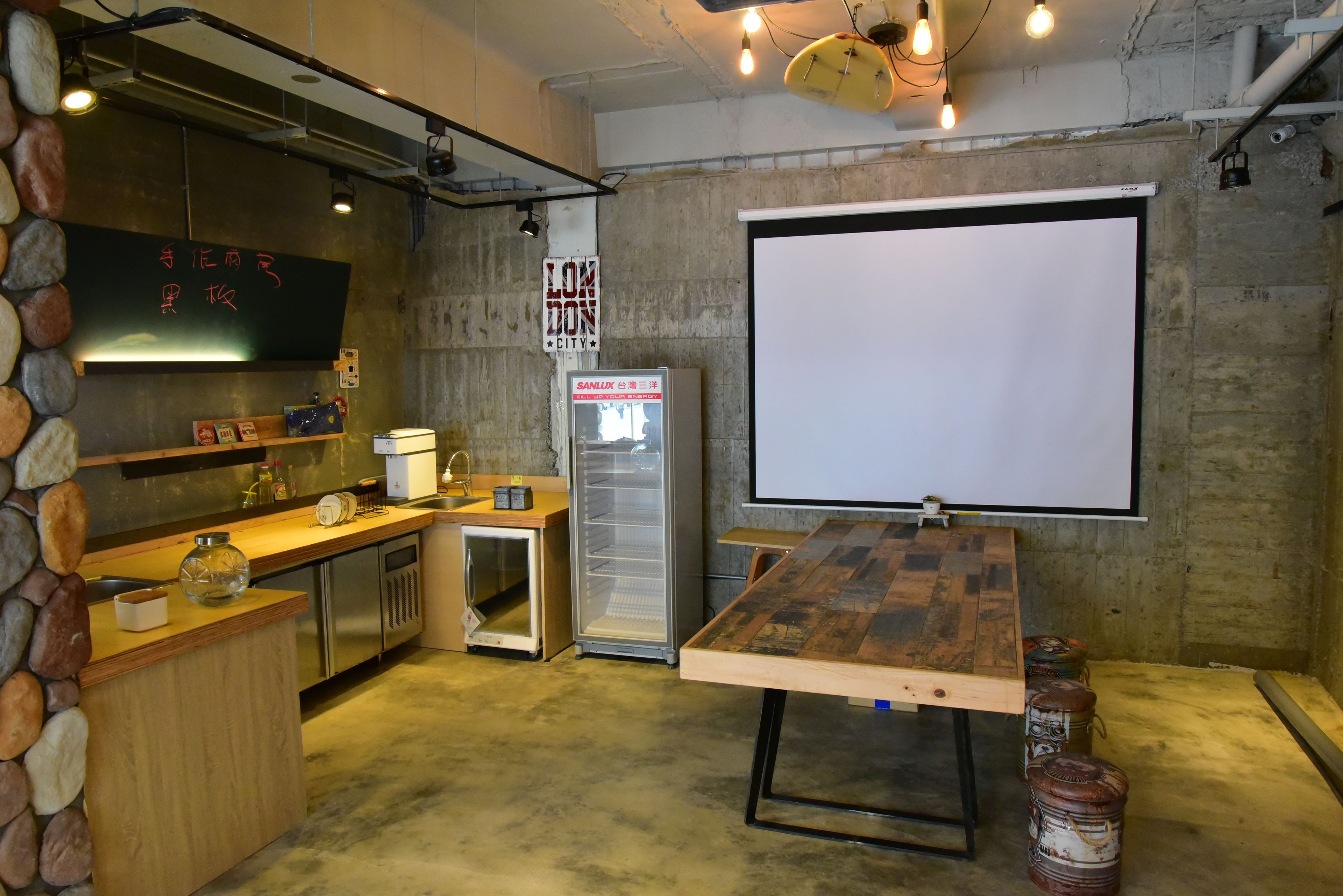 A kitchen with a stone wall, a chalkboard, a refrigerator, and a projector screen.