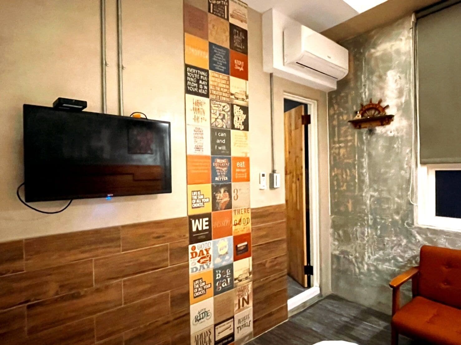 A room with a television mounted on the wall, a wooden floor, and a brick wall.