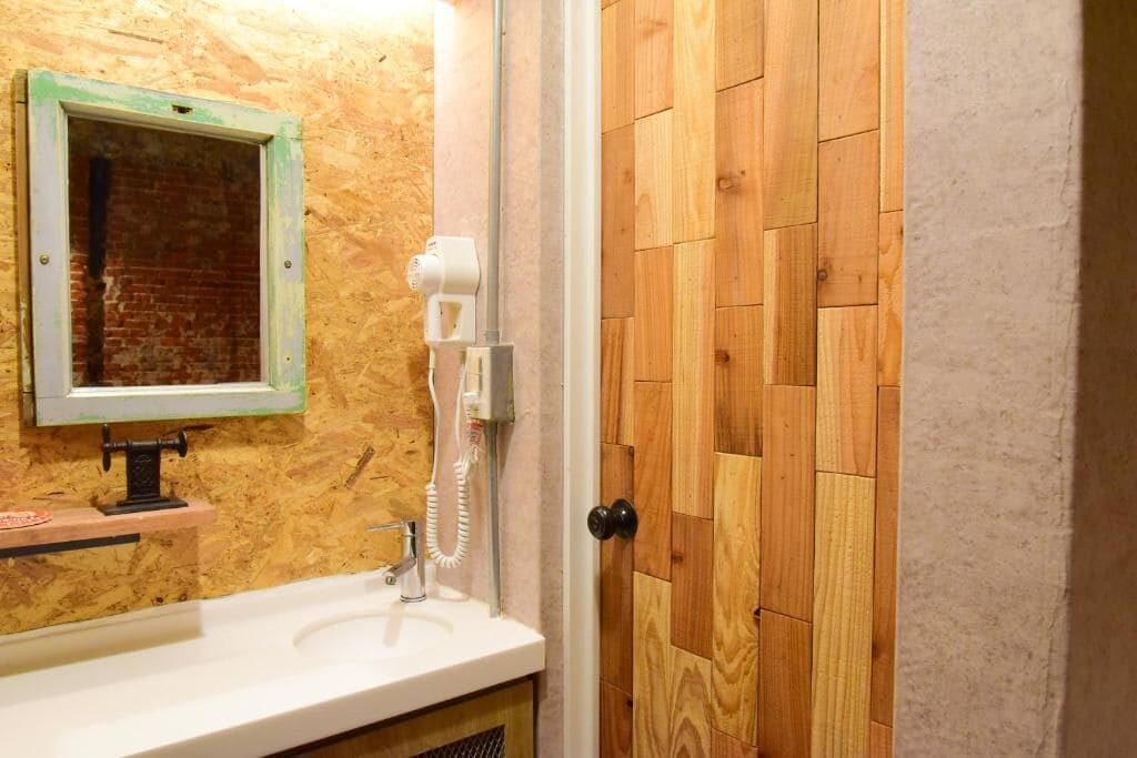 Un baño con pared de madera, un lavabo, un espejo y un secador de pelo.