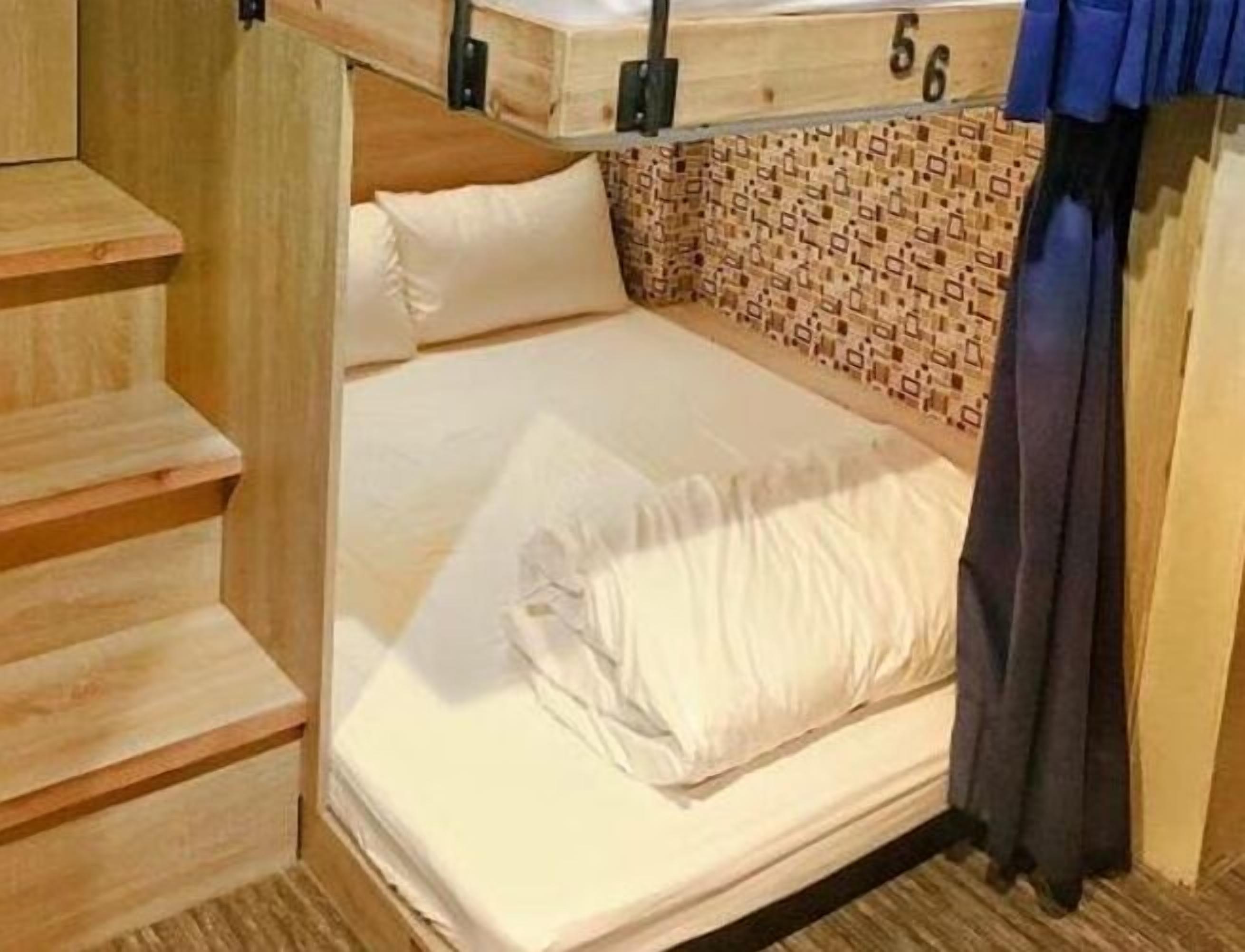 A single bed with a wooden headboard, a patterned wall, and a curtain.