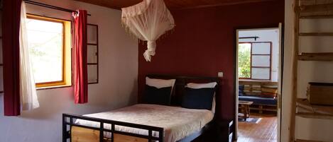 Quarto com cama de madeira, janela com cortinas vermelhas e teto de madeira.