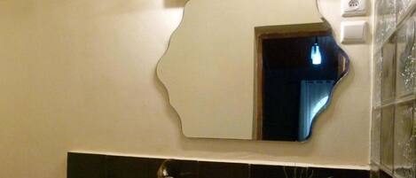 A bathroom with a large mirror, a sink, a faucet, and a potted plant.