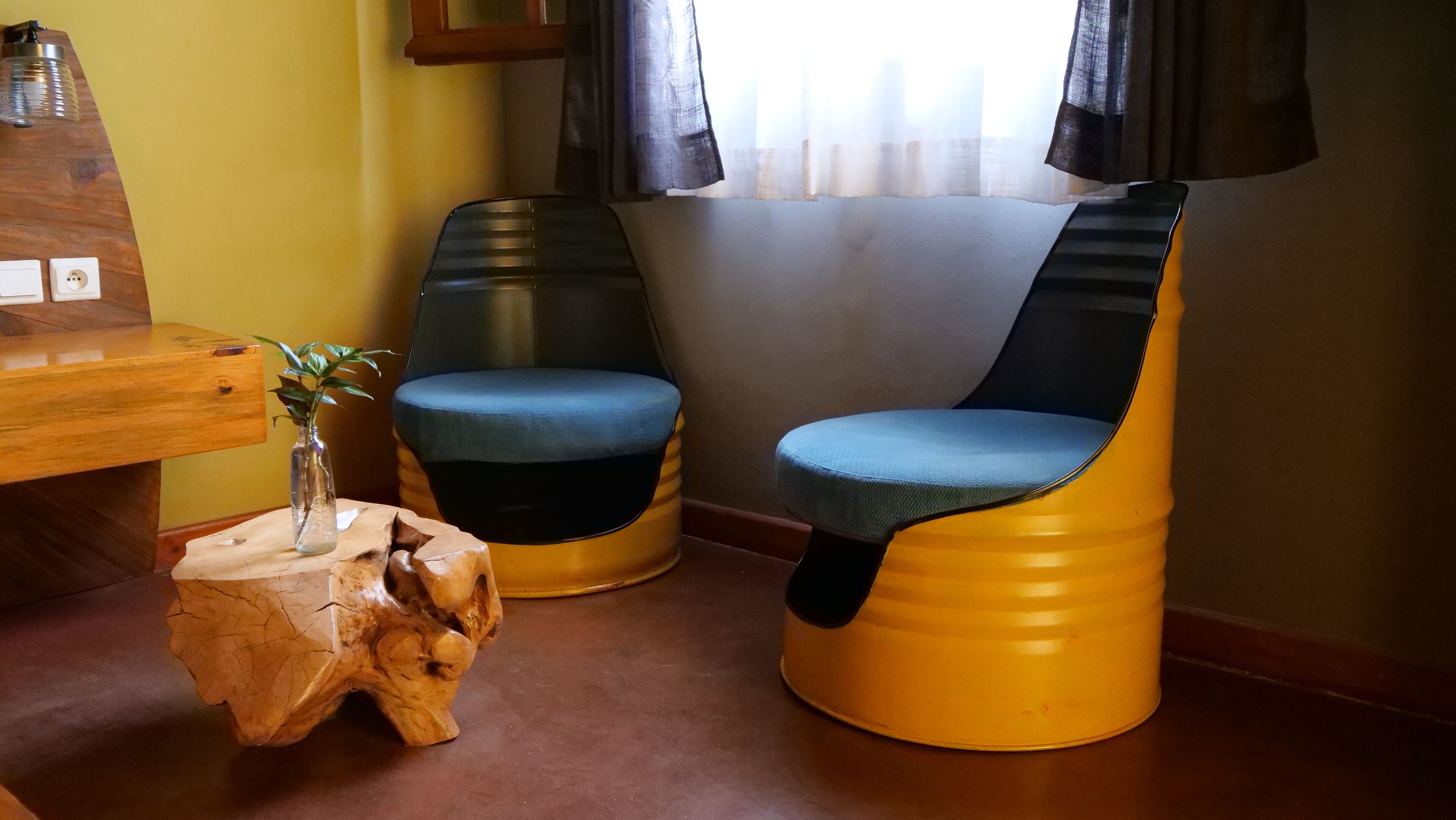 Une pièce avec un bureau en bois, deux chaises modernes, un petit tabouret en bois et une fenêtre avec des rideaux.