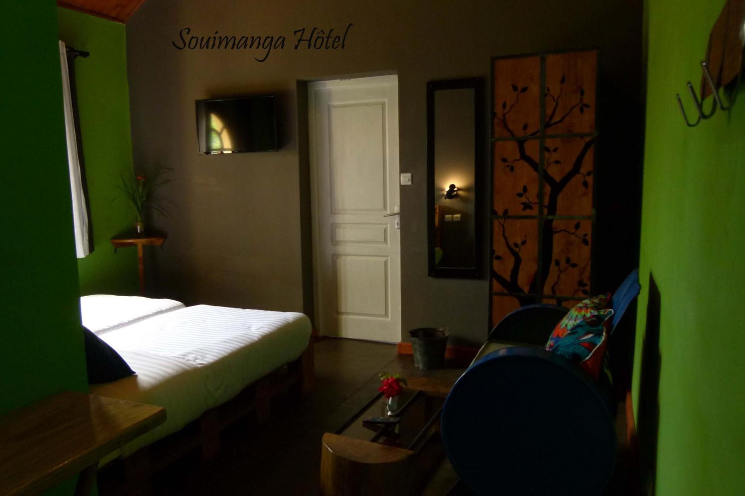 Une chambre d’hôtel comprenant un lit, un bureau, une chaise, une petite table avec un vase et un téléviseur fixé au mur.