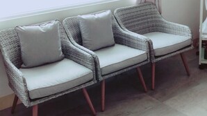 A wicker sofa with cushions against a wall, a window with a curtain, and a tiled floor. - Moon Fish (Magong)