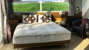 A bedroom with a large bed, a nightstand, a chair, and a view of greenery through a window. - Moon Fish (Magong)