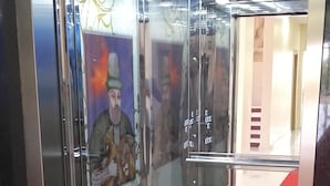 Un ascenseur moderne doté de portes en verre, d’un sol en marbre et d’une fresque murale.