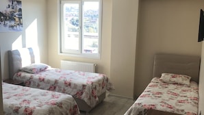 Une chambre avec deux lits, un bureau en bois, un radiateur et une fenêtre donnant sur l’extérieur.