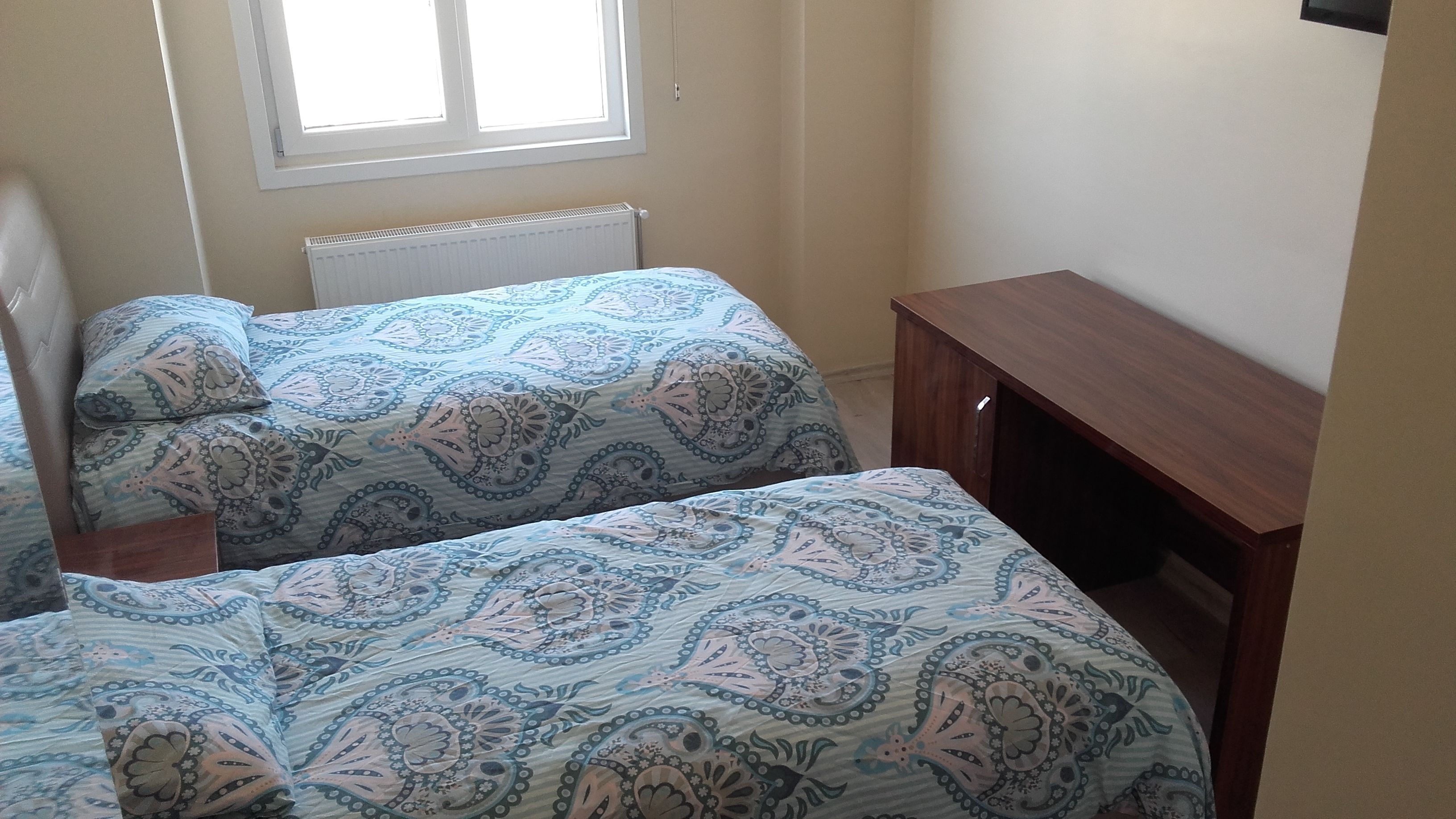 A room with two beds, a wooden nightstand, and a small wooden desk.