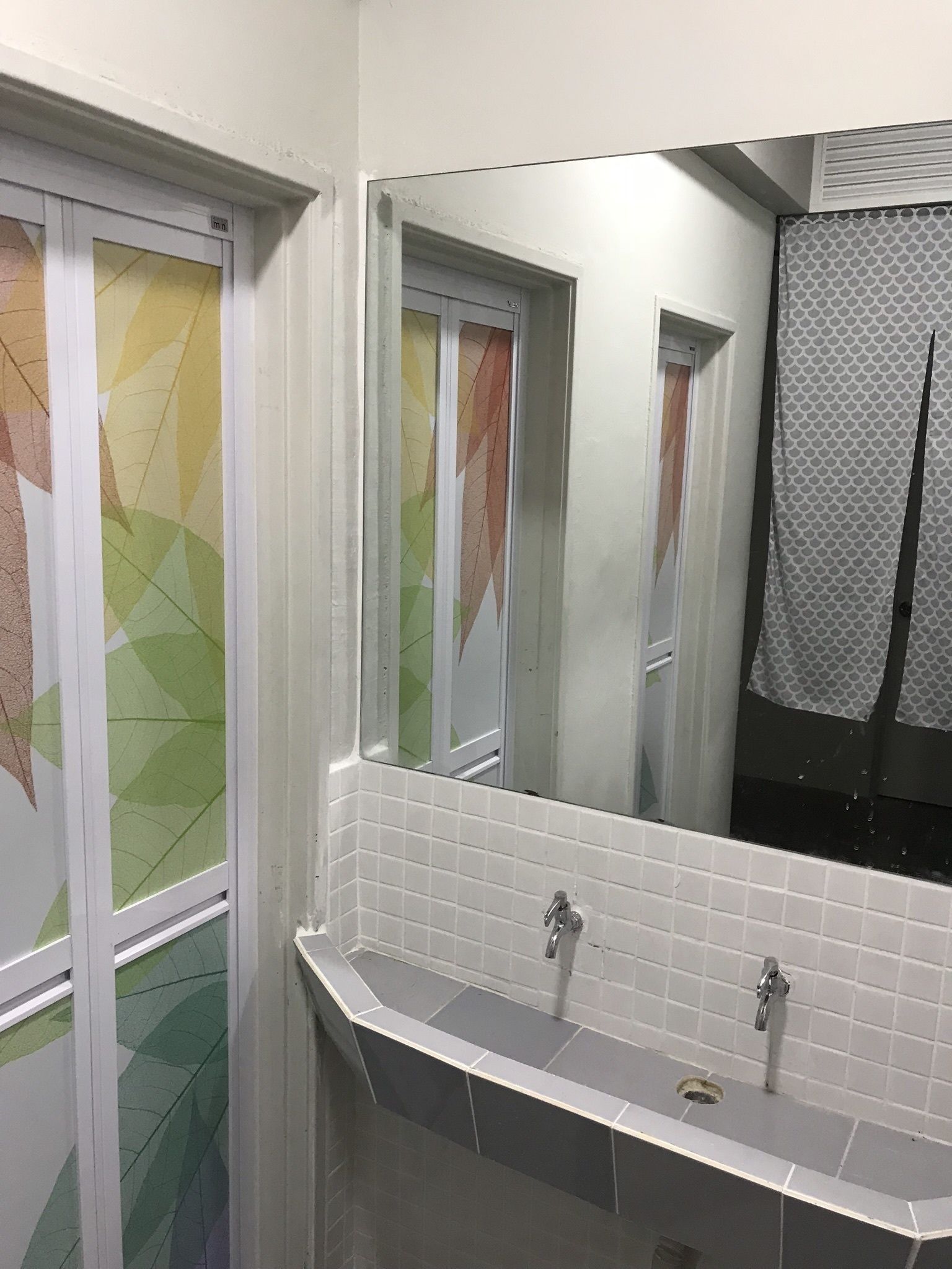 A bathroom with a white tiled wall, a large mirror, and a sink with two faucets.