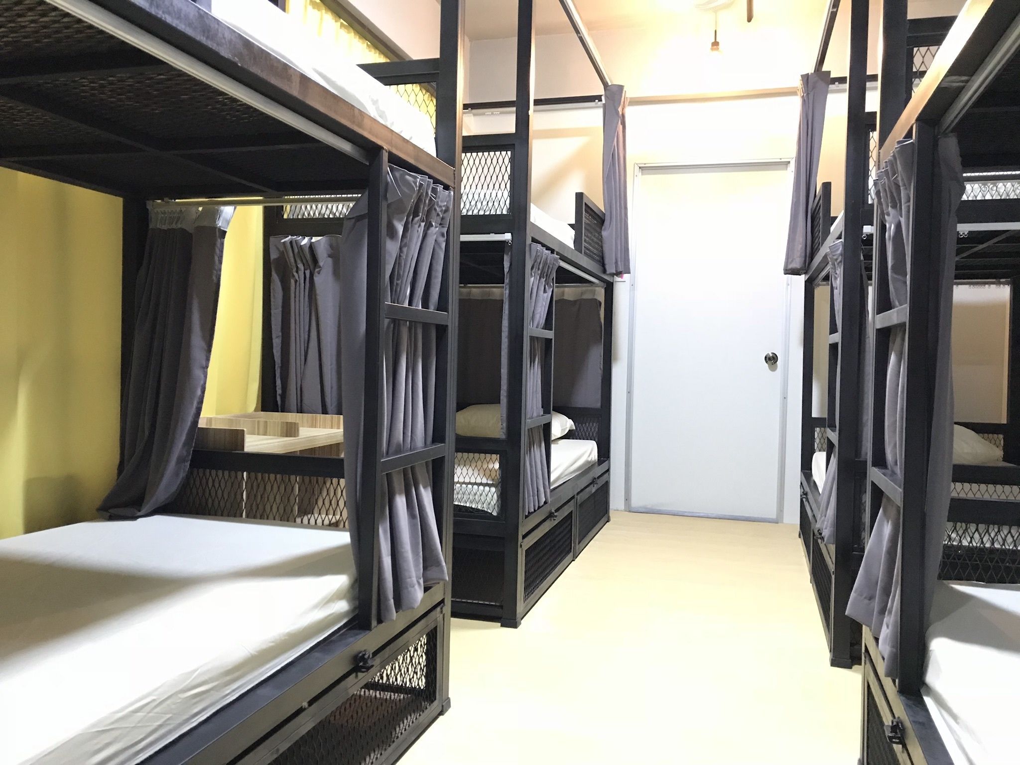 Une chambre de type dortoir, avec des lits superposés, une porte et une fenêtre avec des rideaux.