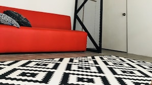 A room with a red sofa, a patterned rug, a white door, and a black metal partition with motivational quotes. - The Good Travelers Hostel - KL Airport (Sepang)