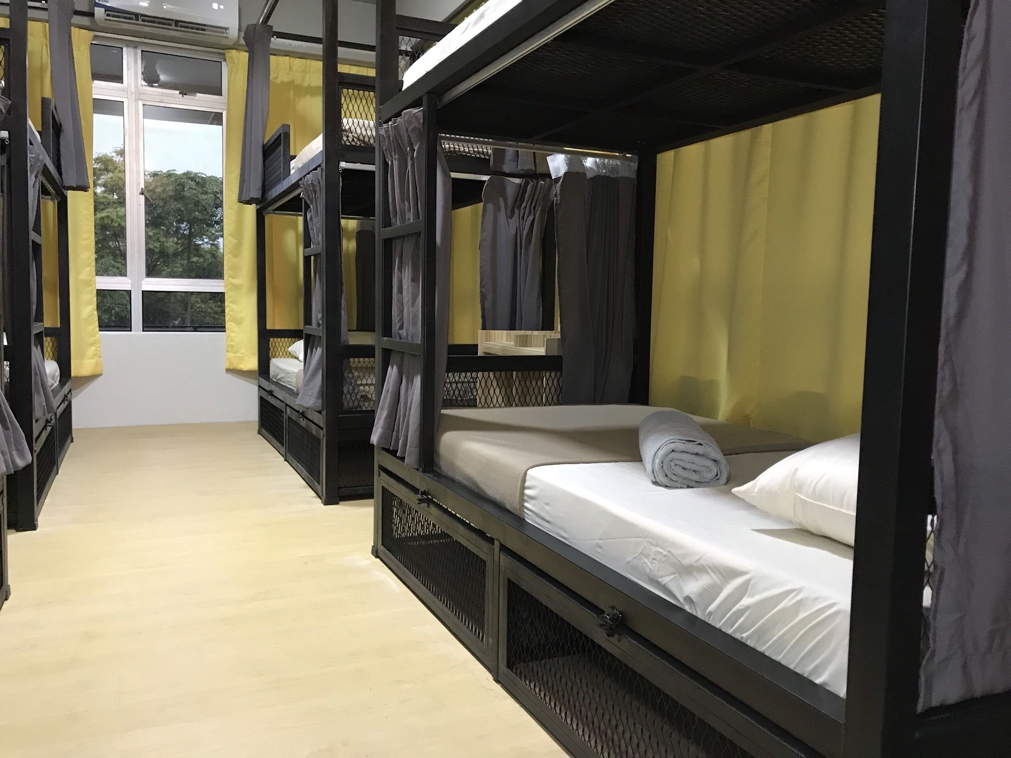 A dormitory-style room with bunk beds, a window, and curtains.