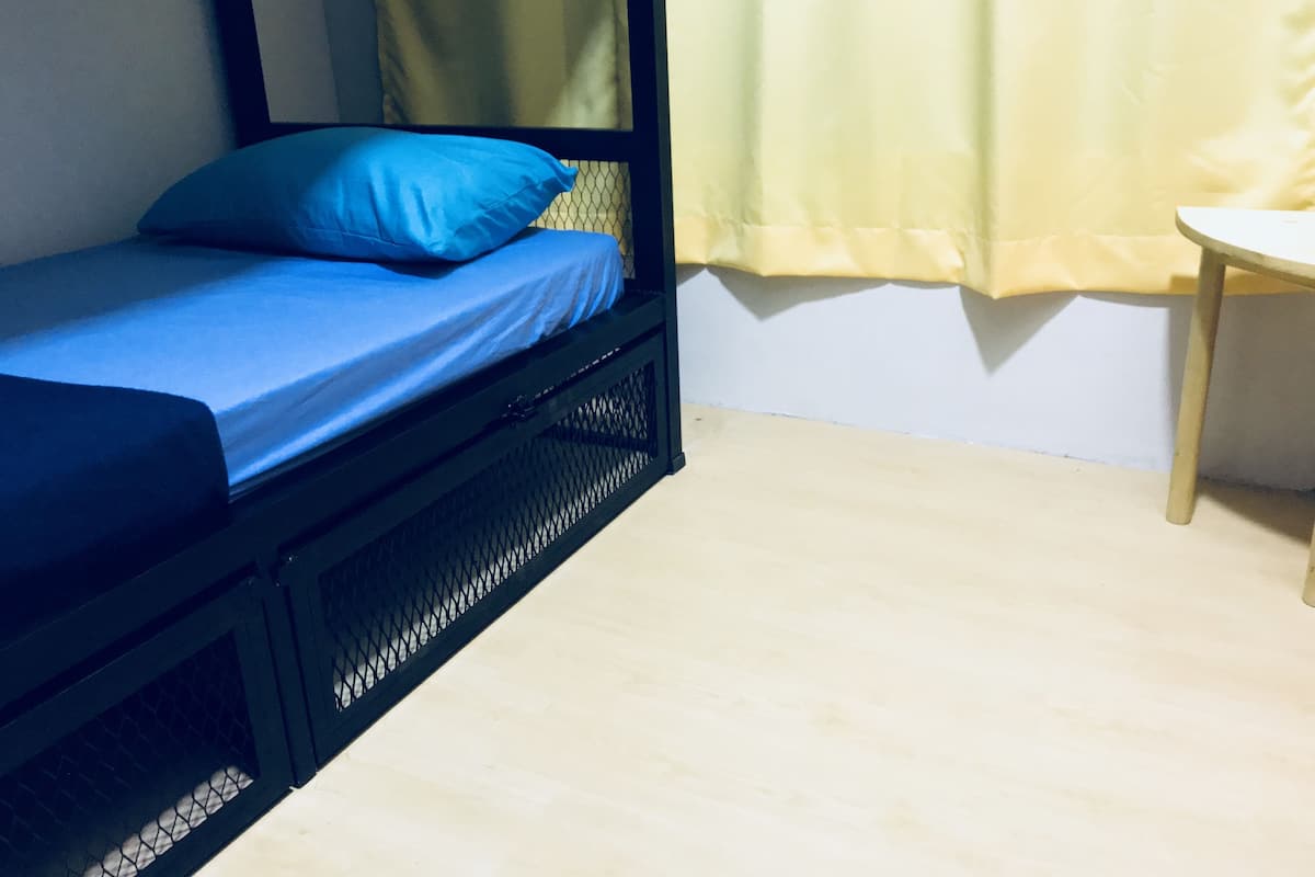 Un lit simple avec un matelas et un oreiller bleus, un cadre en métal noir et un rideau jaune.