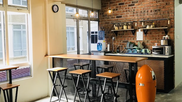 A kitchen with a brick wall, a water dispenser, a toaster, and a vintage orange appliance. - The Good Travelers Hostel - KL Airport (Sepang)