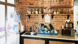 A kitchen with brick walls, a water dispenser, a coffee machine, and shelves with jars. - The Good Travelers Hostel - KL Airport (Sepang)