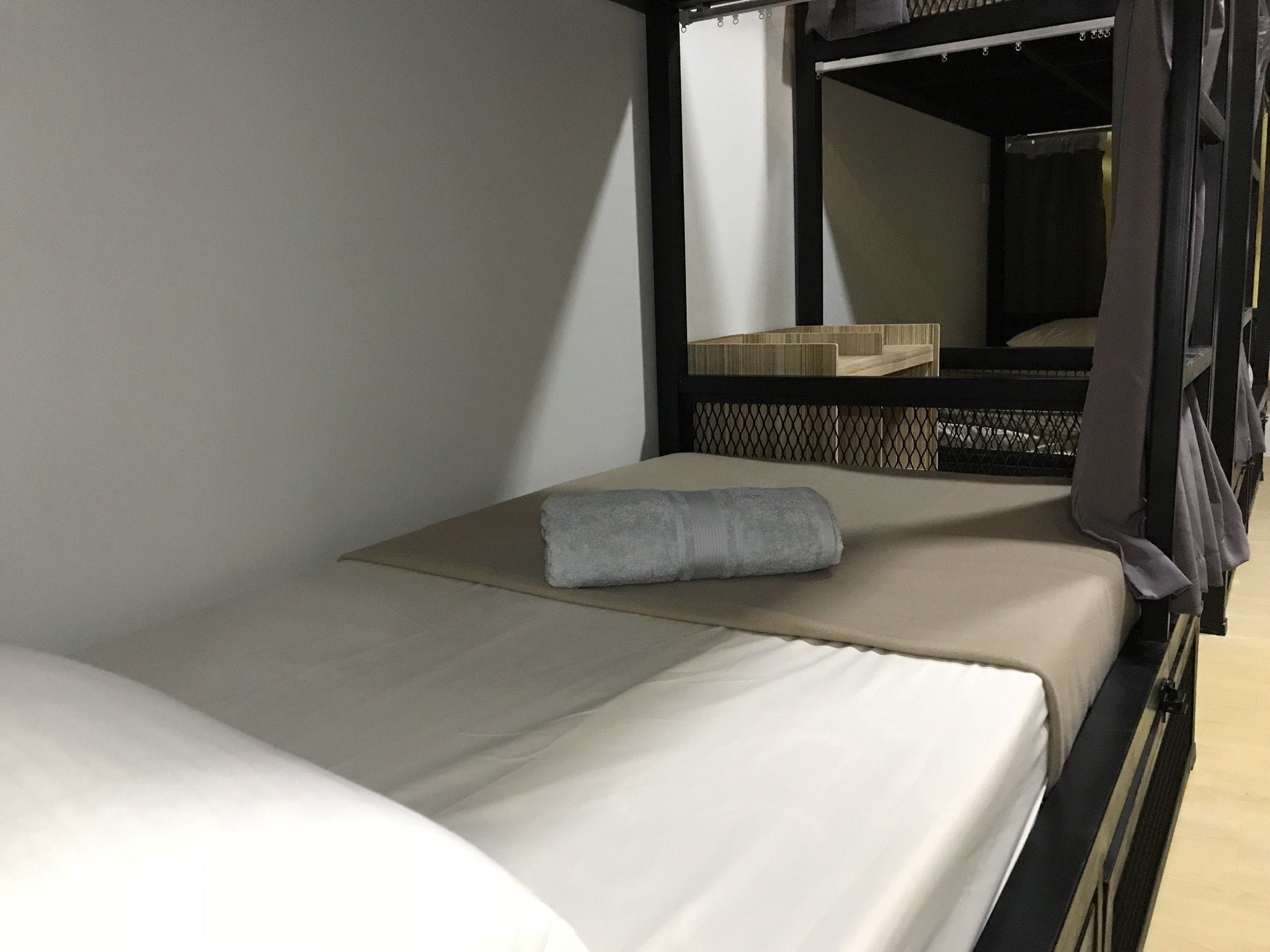 A single bed with a grey towel, a wooden headboard, and a mirror above it.