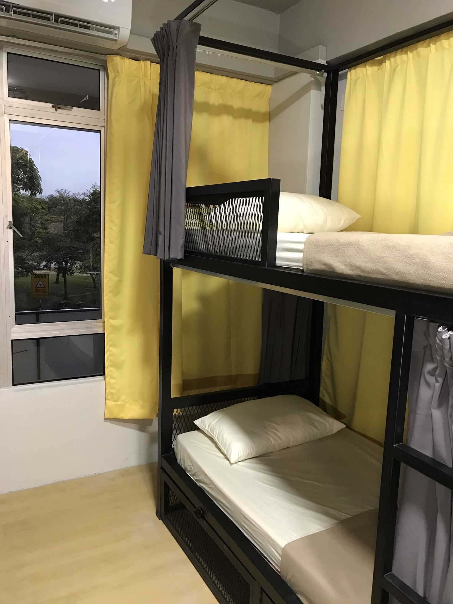 Dormitorio con literas, cortinas amarillas, una ventana y vistas a árboles desde afuera.