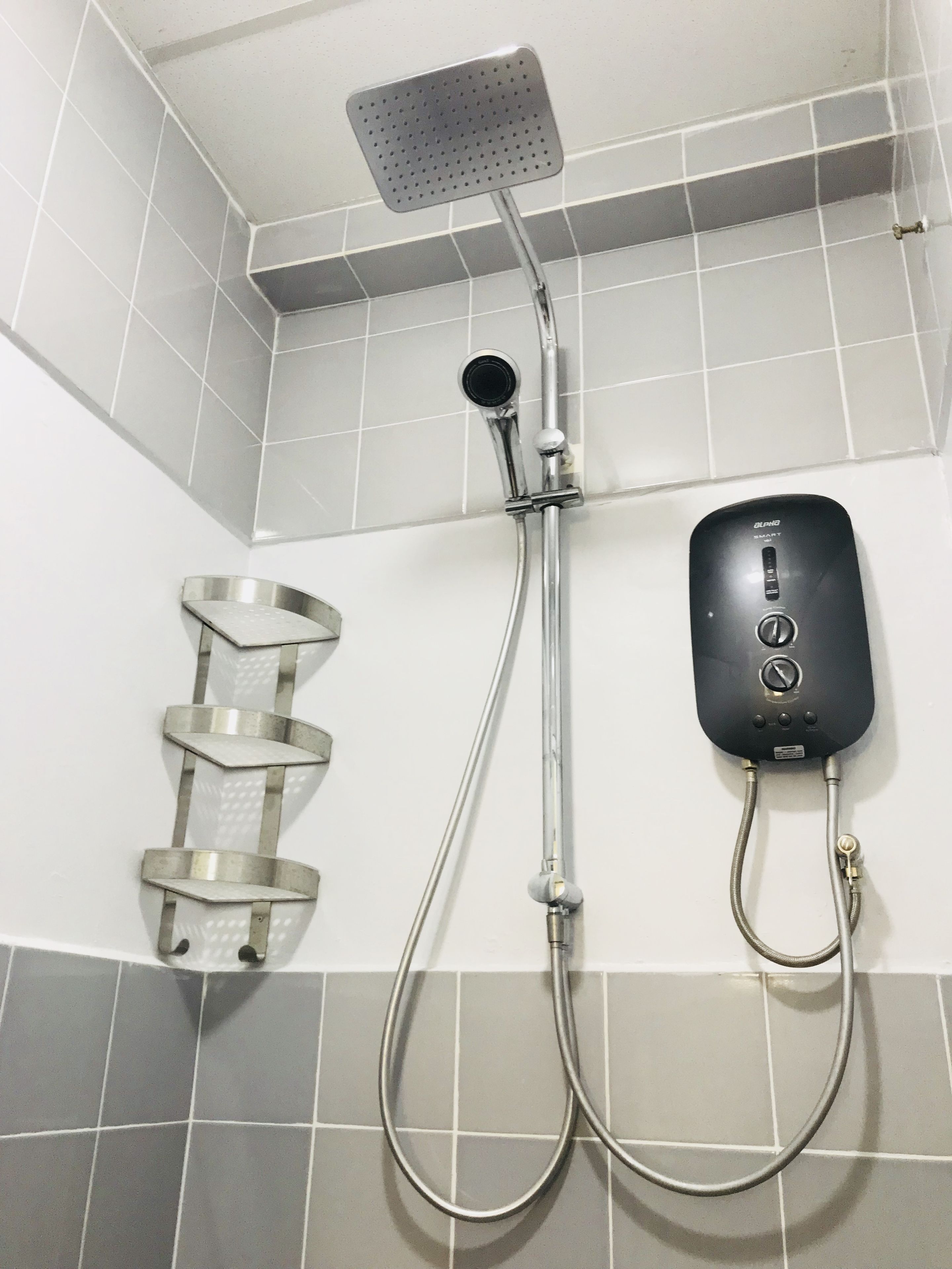 A shower with a handheld showerhead, a wall-mounted control panel, and a step stool.