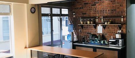 A modern kitchen with a brick wall, a wooden bar counter, and a coffee machine.