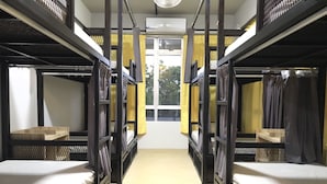 A dormitory room with bunk beds, a window with yellow curtains, and an air conditioning unit on the wall. - The Good Travelers Hostel - KL Airport (Sepang)