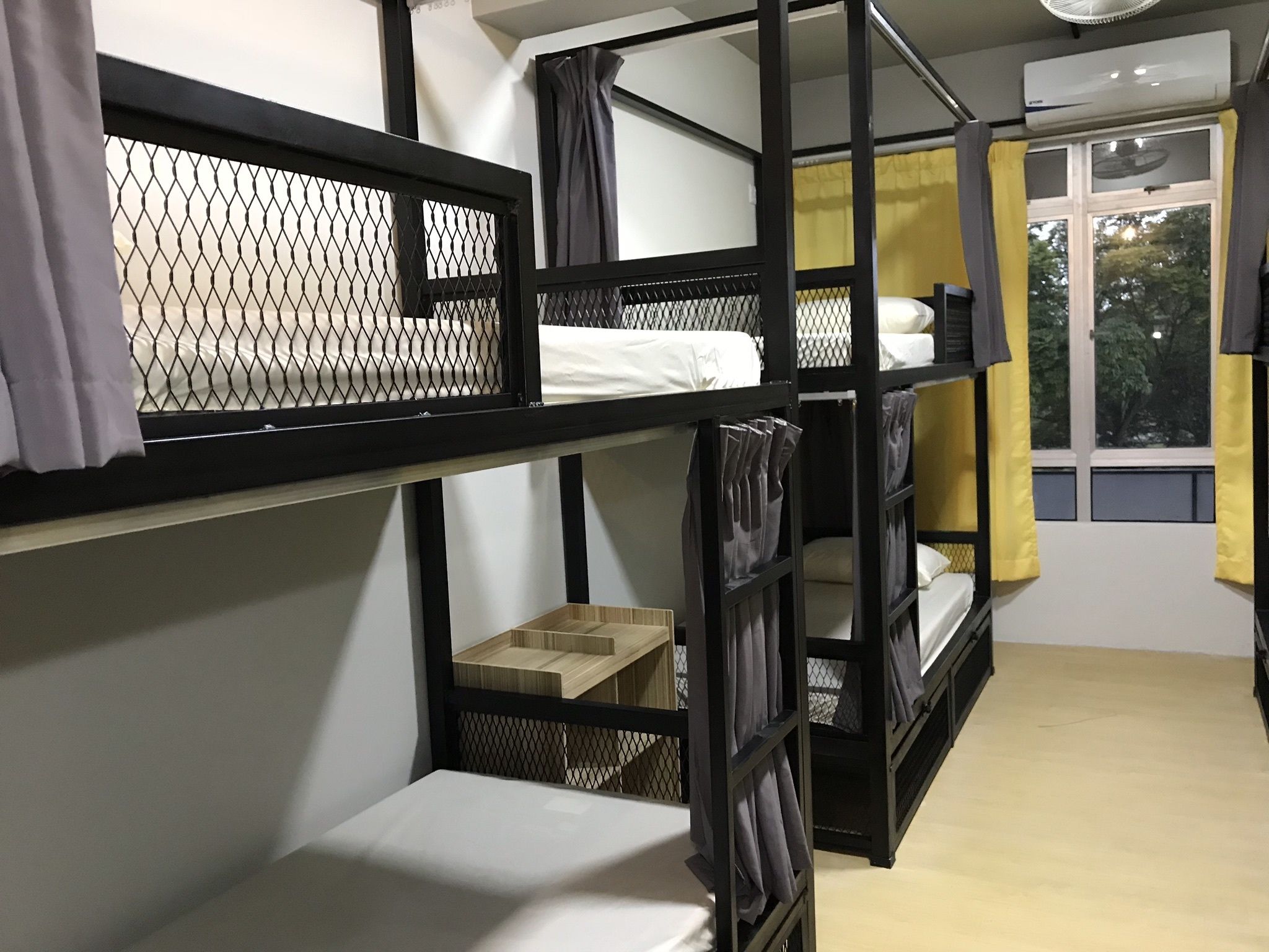 A dormitory room with bunk beds, a window with curtains, and an air conditioning unit.