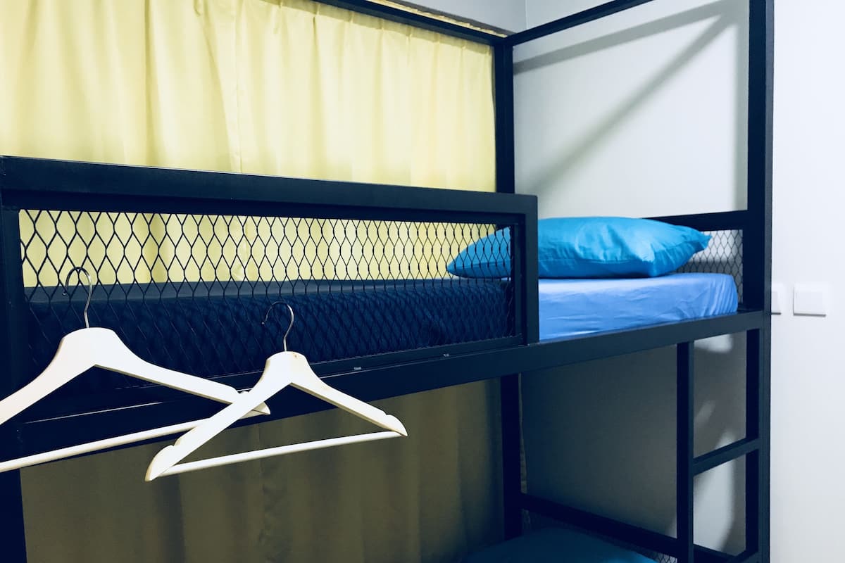 Un lit superposé avec un couchage supérieur protégé par un moustiquaire, un oreiller bleu et un cintre blanc.