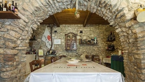 A stone-walled dining area with a table set for a meal, a flag, and shelves with bottles.